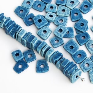 May include: A string of blue ceramic beads with a square shape and a hole in the center. The beads are arranged in a line and are strung on a wire. There are also loose blue ceramic beads scattered around the string.
