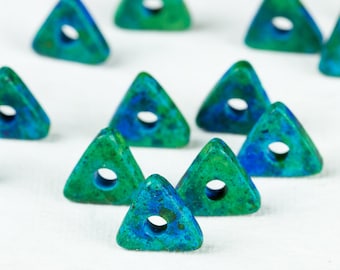 May include: A group of green and blue triangular beads with a hole in the center. The beads are scattered on a white surface.