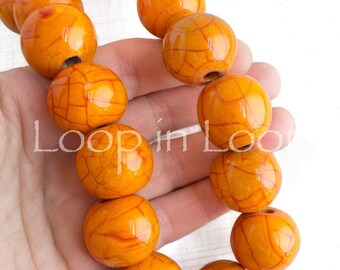 May include: A strand of orange ceramic beads with a crackled glaze finish. The beads are round and have a hole in the centre for stringing.