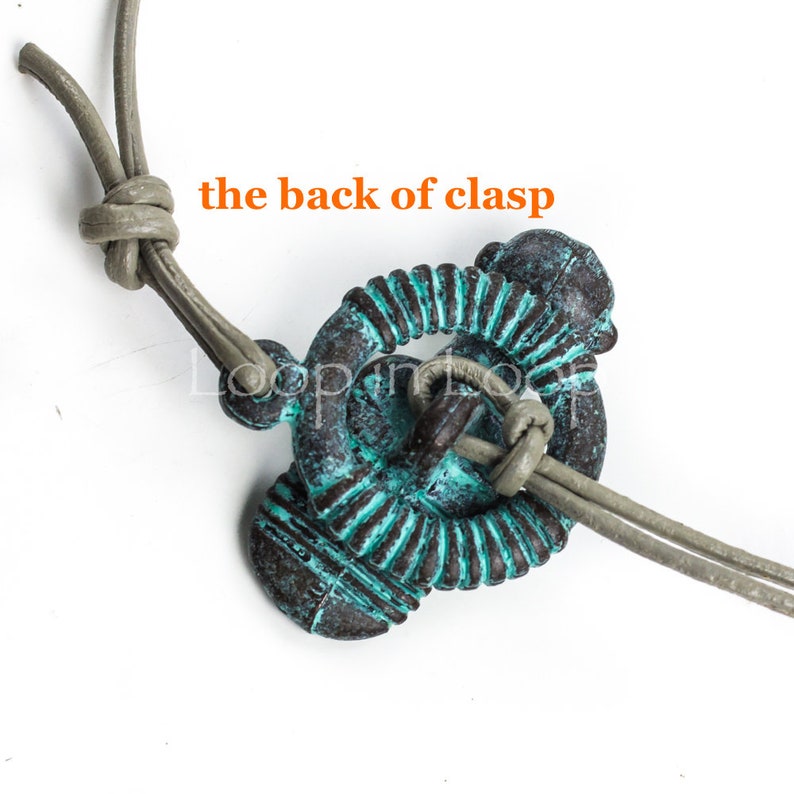 May include: A close-up of a turquoise and brown metal clasp with a grey leather cord threaded through it. The text "the back of clasp" is visible in the image.