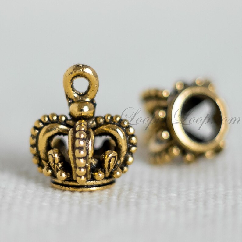May include: Two gold-toned metal crown-shaped charms with a loop at the top. The charms are detailed with small beads and decorative elements.