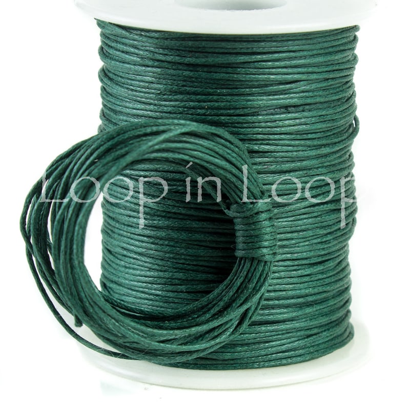 May include: A spool of dark green cord wrapped around a white plastic cylinder. The cord is wound tightly in horizontal layers, with a loose loop of the same dark green cord hanging in front. The text Loop in Loop is printed across the center.