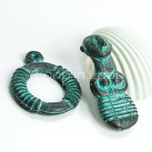 May include: Two antique-looking metal charms in a teal green color. One charm is a ring with a textured surface and the other is a small figurine with a human-like shape.