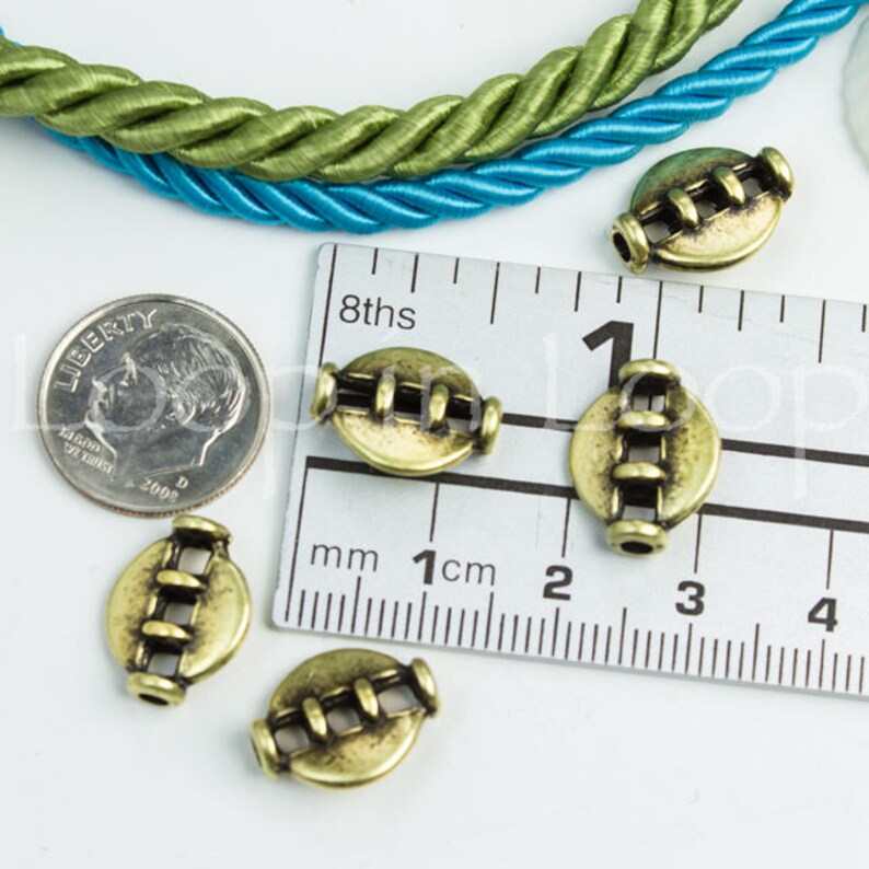 May include: Five antique gold-toned metal beads with a decorative design. The beads are approximately 1 cm in diameter and are arranged on a ruler.