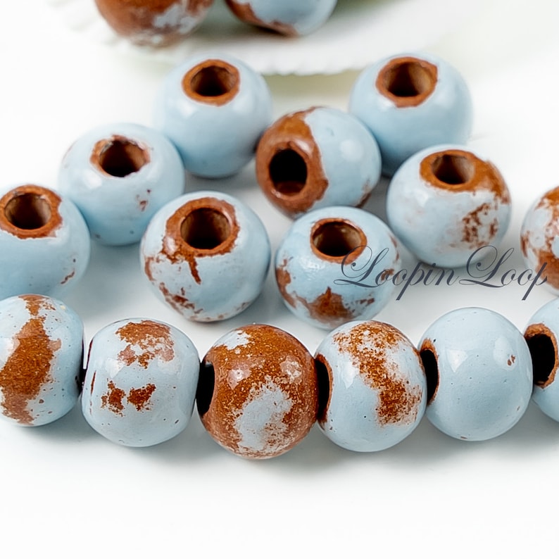 May include: A collection of light blue ceramic beads with brown speckles. The beads have a hole in the centre for stringing.