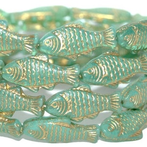 May include: A strand of green glass beads shaped like fish with gold accents. The beads are strung together and have a glossy finish.