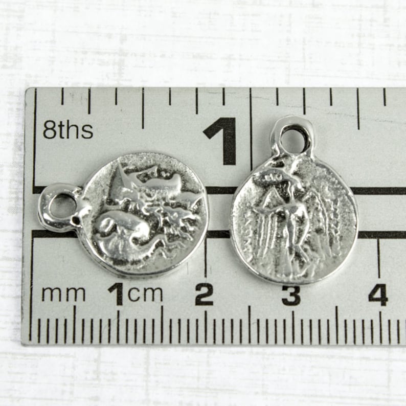 May include: Two silver-toned metal charms, each with a different design. One charm features a winged angel, while the other depicts a mythical creature. Both charms are approximately 1 cm in diameter and have a small loop for attaching to a necklace or bracelet.