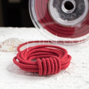 May include: A close-up of a spool of red cord. The cord is wound tightly and has a smooth, even texture.
