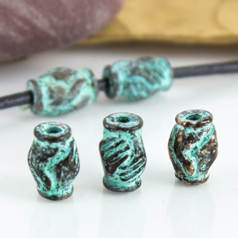 May include: Four turquoise green and brown metal beads with a hand-shaped design. The beads are round and have a textured surface.