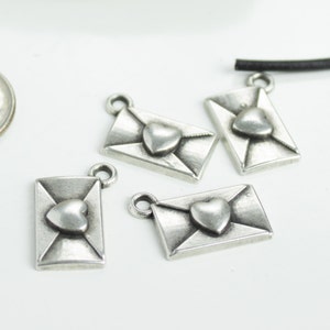 May include: Four silver-toned metal charms shaped like envelopes with a heart in the centre. The charms are perfect for jewellery making or scrapbooking.