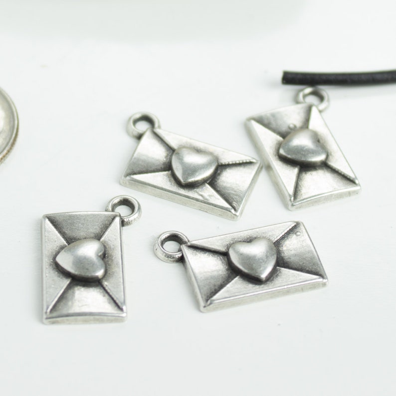 May include: Four silver-toned metal charms shaped like envelopes with a heart in the centre. The charms are perfect for jewellery making or scrapbooking.