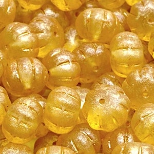 May include: A close-up of a pile of gold-colored glass beads. The beads are round and have a textured surface. They are perfect for jewelry making or other craft projects.