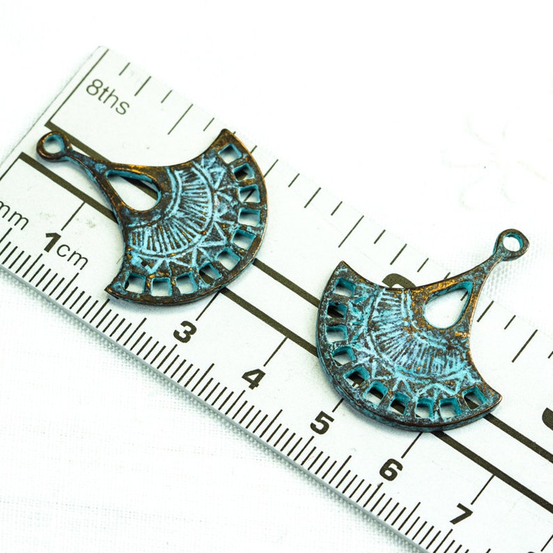 Puede incluir: Dos abalorios de metal en forma de abanico de color azul turquesa con un dise&ntilde;o decorativo de corte. Los abalorios tienen un bucle en la parte superior para sujetarlos a joyas u otras manualidades. Los abalorios miden aproximadamente 5 cm de largo.