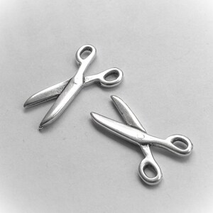 May include: Two silver-toned metal scissor charms. The charms are about 1 inch long and have a detailed design.