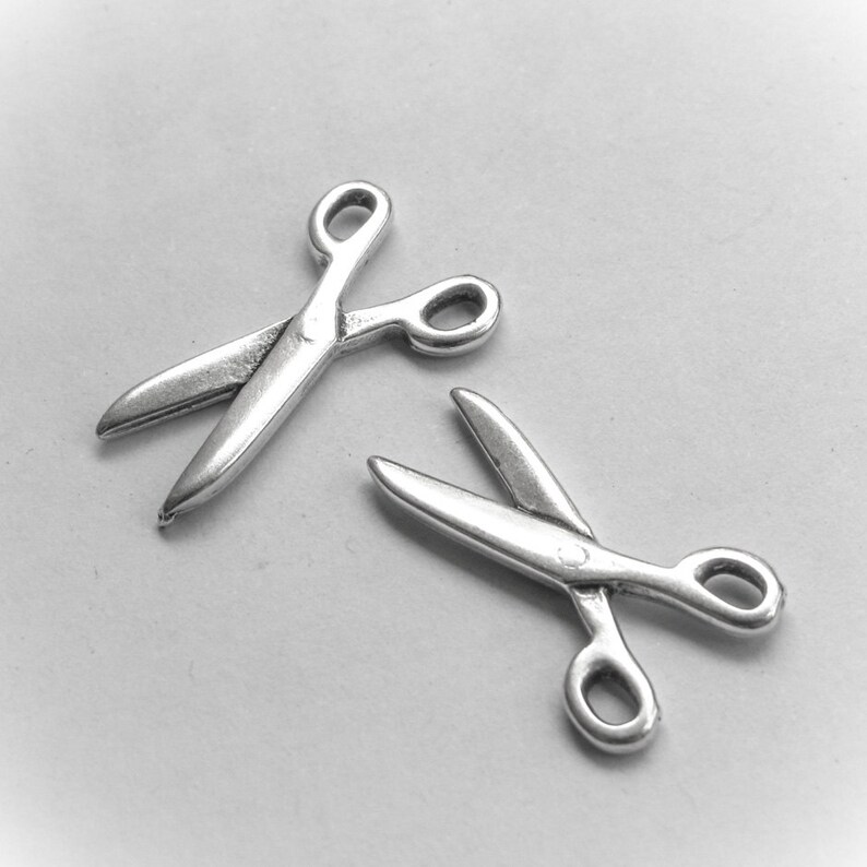 May include: Two silver-toned metal scissor charms. The charms are about 1 inch long and have a detailed design.