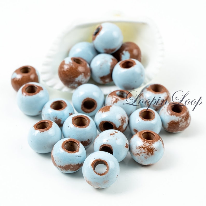 May include: A collection of light blue wooden beads with brown speckles. The beads have a hole in the centre for stringing.