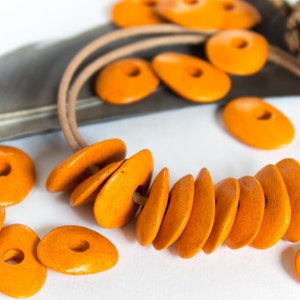 May include: A necklace made of orange wooden beads. The beads are oval shaped and have a smooth, polished finish. The necklace is strung on a brown leather cord.