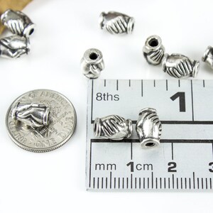 May include: Silver tone metal beads with a handshake design. The beads are approximately 1 cm in diameter and are shown next to a ruler for size reference.