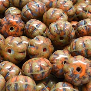 May include: Close-up of a pile of ceramic beads. The beads are a mix of orange, brown, and blue colors. Each bead has a unique shape with a hole for stringing. The beads have a glossy finish.