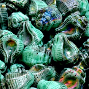 May include: A close-up of a pile of green glass seashells with iridescent details. The shells are smooth and have a textured surface.