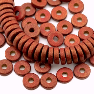 May include: Red and gold-toned wooden beads with a donut shape. The beads are strung together in a necklace and scattered on a white surface. The beads have a rustic, textured appearance, suitable for jewelry making.