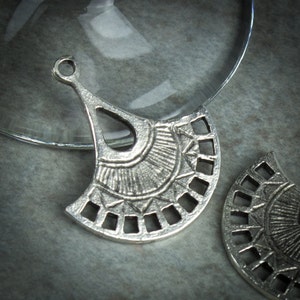 Puede incluir: Dos colgantes de metal plateado en forma de abanico con un dise&ntilde;o geom&eacute;trico. Los colgantes tienen un agujero en la parte superior para sujetarlos a un collar o pulsera.