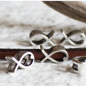 May include: Four silver charm pendants in the shape of a fish with a heart inside. The charms are on a brown leather strap.