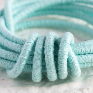 May include: Close-up of a light blue, tightly woven, rope-like cord, twisted into a circular shape.