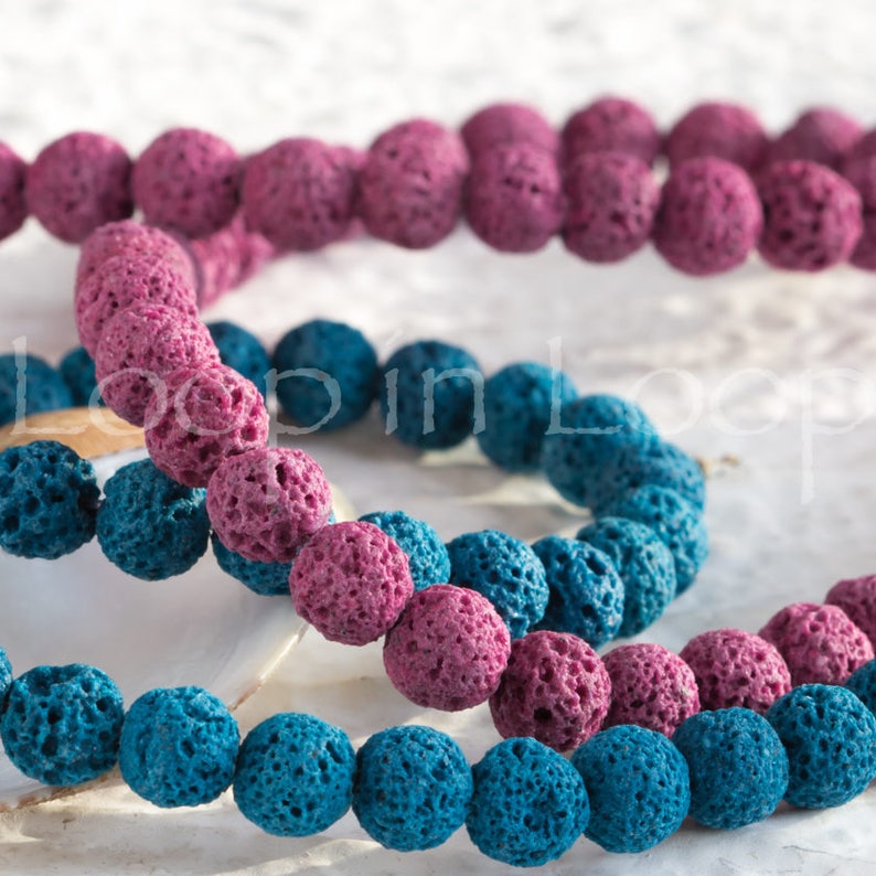 May include: Two strands of lava rock beads, one in pink and one in blue. The beads are round and have a rough, porous texture.
