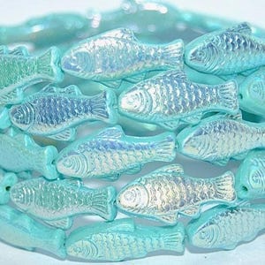 May include: A wrap bracelet composed of multiple turquoise-colored beads shaped like small fish. Each bead features a pearlescent, iridescent finish that reflects light, creating a shimmering effect across the entire circular structure.