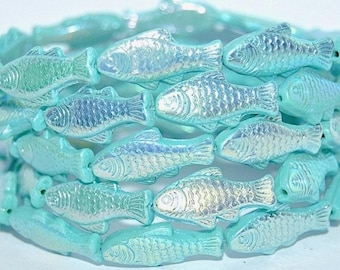 May include: A wrap bracelet composed of multiple turquoise-colored beads shaped like small fish. Each bead features a pearlescent, iridescent finish that reflects light, creating a shimmering effect across the entire circular structure.