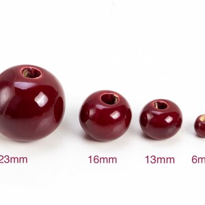 Op de afbeelding: Vier rode keramische kralen in verschillende maten. De kralen meten 23 mm, 16 mm, 13 mm en 6 mm.