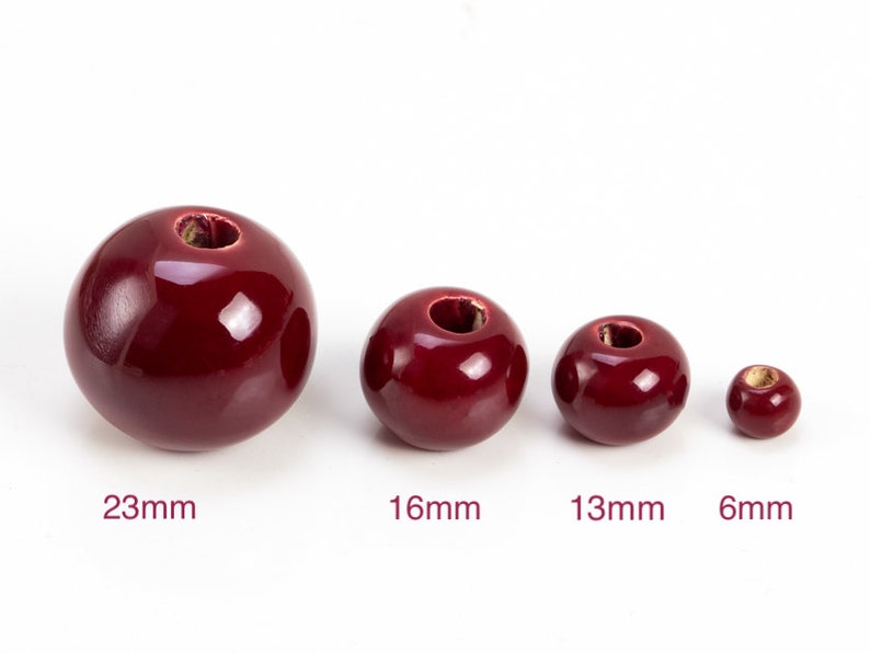 Op de afbeelding: Vier rode keramische kralen in verschillende maten. De kralen meten 23 mm, 16 mm, 13 mm en 6 mm.
