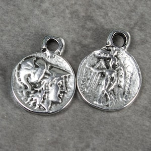 May include: Two silver charm pendants with a raised design of a mythological figure. The pendants have a loop at the top for attaching to a chain or bracelet.