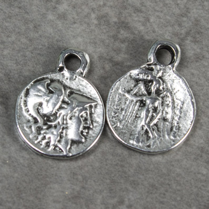 May include: Two silver charm pendants with a raised design of a mythological figure. The pendants have a loop at the top for attaching to a chain or bracelet.