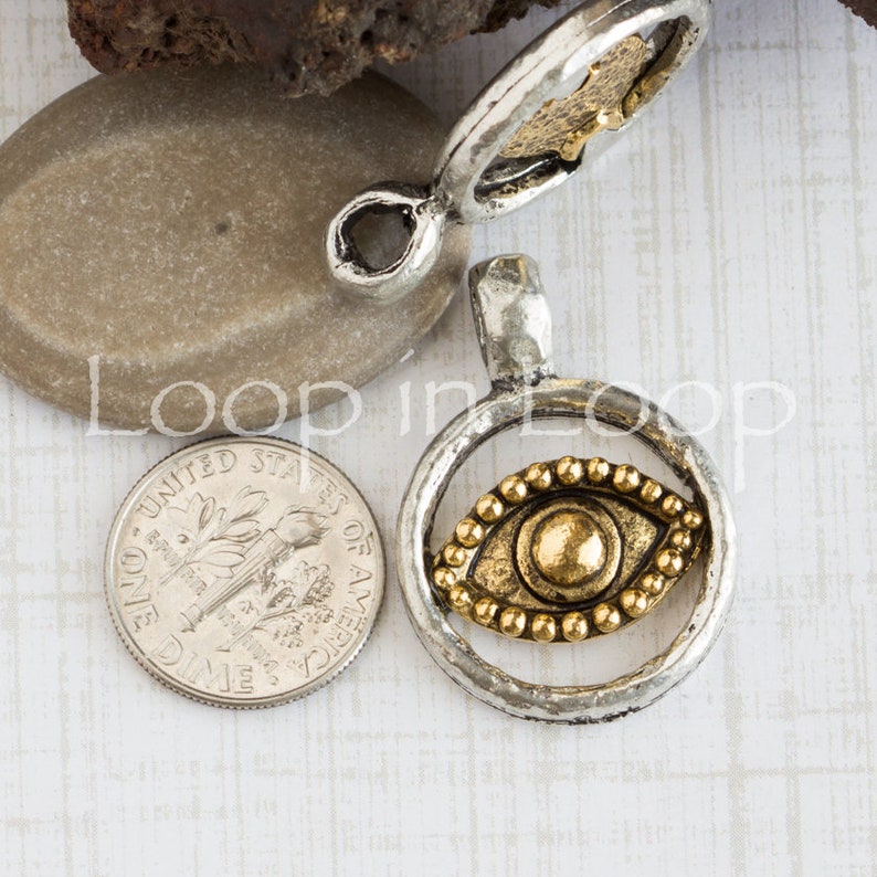 May include: Silver pendant with a gold eye charm inside a circle. The eye has a gold bead border. The pendant is about the size of a US dime.