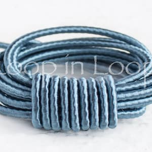 May include: A bundle of light blue cord, looped and secured with a matching cylindrical clasp. The cord appears to be made of a woven material, and the clasp has a ribbed texture. The text "Loop in Loop" is partially visible.