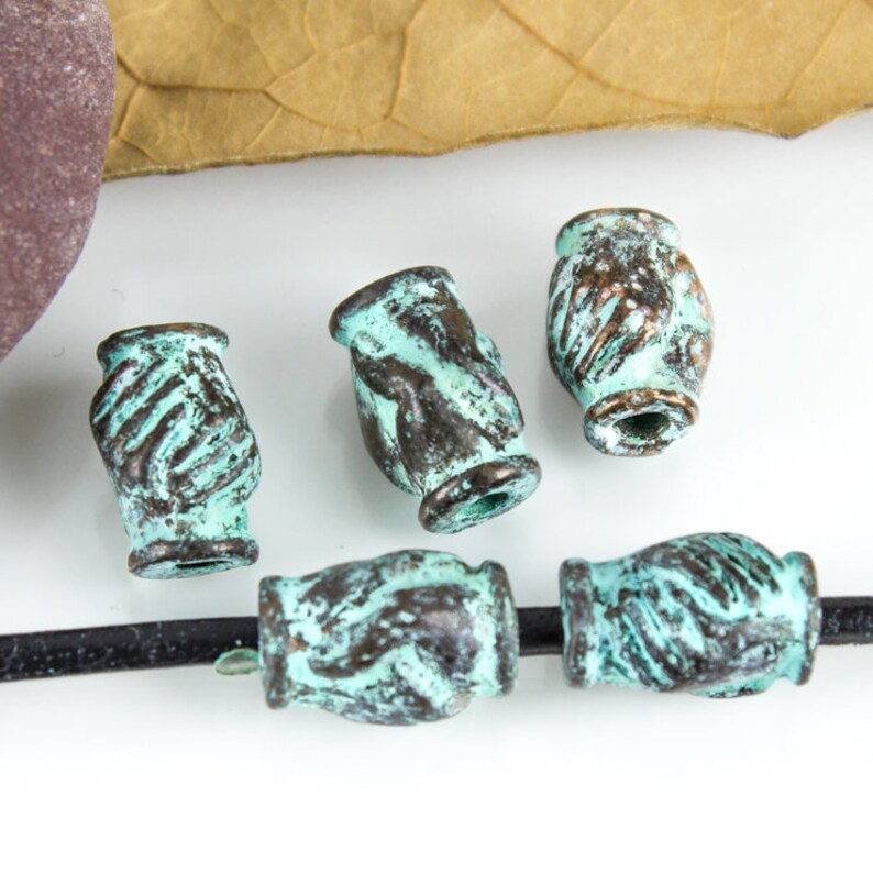 May include: Five turquoise and brown metal beads with a hand-shaped design. The beads are arranged in a row on a black surface.