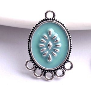 May include: Silver-toned pendant with a light blue enamel oval featuring a silver-toned embossed design. The pendant has a loop at the top and a decorative border of five silver-toned rings.