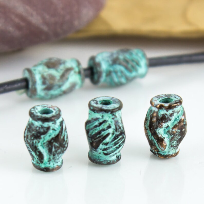 May include: Four turquoise green metal beads with a textured design. The beads are cylindrical and have a slightly rounded shape.
