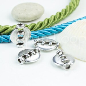May include: Four silver metal beads with a decorative design. The beads have a hole in the center and are designed to be used for jewelry making or other crafts.