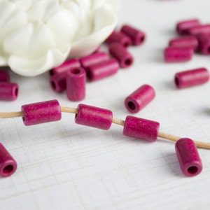 Puede incluir: Una hebra de cuentas de madera rosa con un hilo de fibra natural. Las cuentas son cil&iacute;ndricas y tienen una textura ligeramente rugosa.
