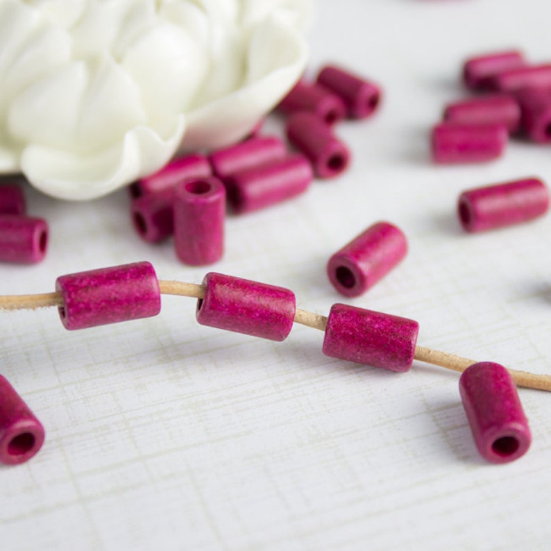 Puede incluir: Una hebra de cuentas de madera rosa con un hilo de fibra natural. Las cuentas son cil&iacute;ndricas y tienen una textura ligeramente rugosa.
