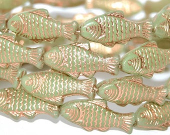 May include: A strand of green glass fish beads with a copper metallic finish. The beads are shaped like fish with detailed scales and fins.