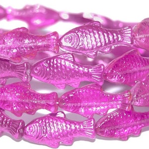 May include: A stack of pink, fish-shaped beads forms a bracelet. The translucent beads are a vibrant magenta color, with details like fins and scales visible. The bracelet is likely made of plastic or a similar material.
