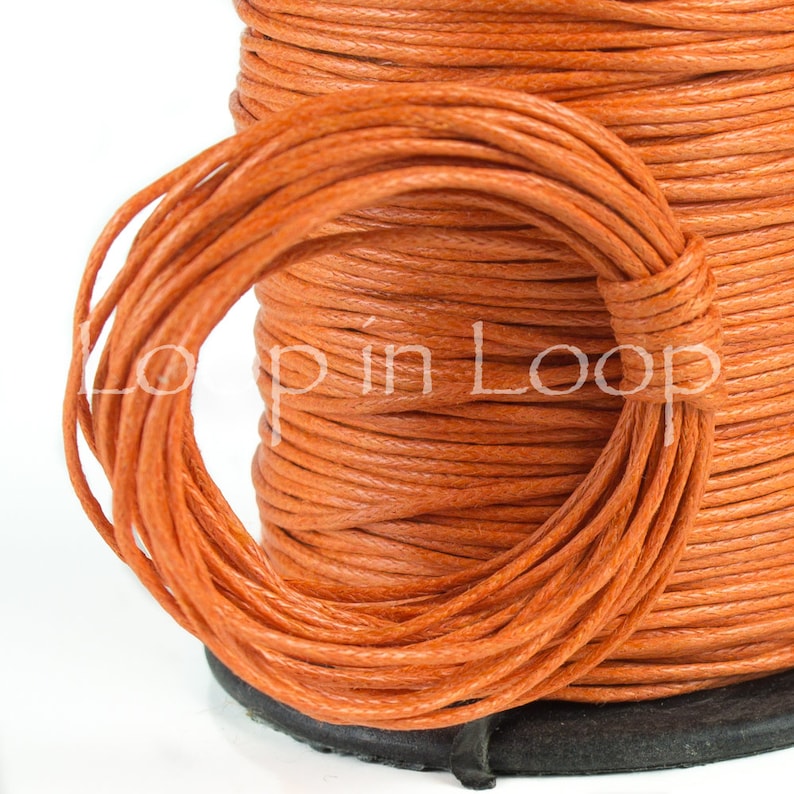 May include: A spool of vibrant orange cord wrapped in a continuous coil, featuring a textured, fibrous surface. The text "Loop in Loop" is overlaid in white across the center of the orange cord, which is wound around a black circular base.