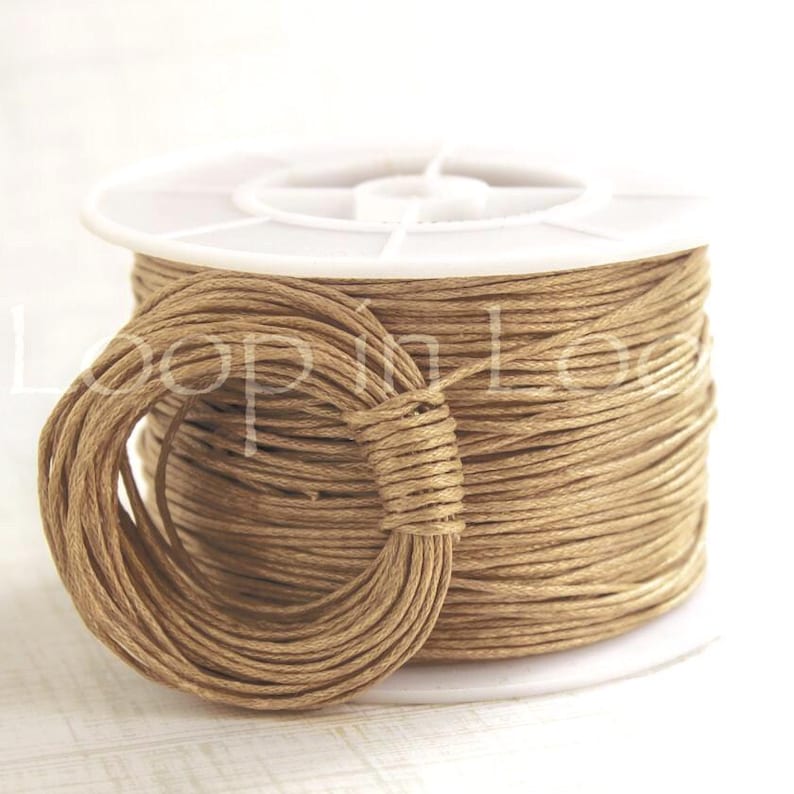 May include: A spool of light brown cord wrapped around a white plastic reel. A separate loop of the same light brown cord is positioned in front of the spool, secured by a small section of the cord wrapped tightly around the bundle.