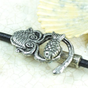 May include: Silver tone pendant featuring an octopus with a fish in its tentacles. The pendant is attached to a black leather cord.