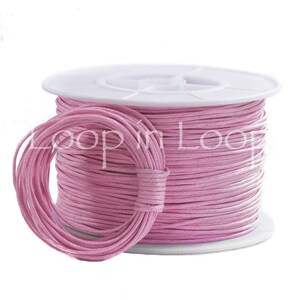 May include: A spool of light pink cord wrapped around a white plastic reel, with a smaller circular coil of the same pink cord resting in front. The text Loop in Loop is overlaid in white across the center of the pink cord spool.