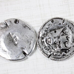 K&ouml;nnte beinhalten: Zwei silberfarbene Metall-M&uuml;nzenanh&auml;nger mit einem Loch zum Aufh&auml;ngen. Ein Anh&auml;nger zeigt ein detailliertes Design eines Frauenprofils, w&auml;hrend der andere Anh&auml;nger schlicht ist.